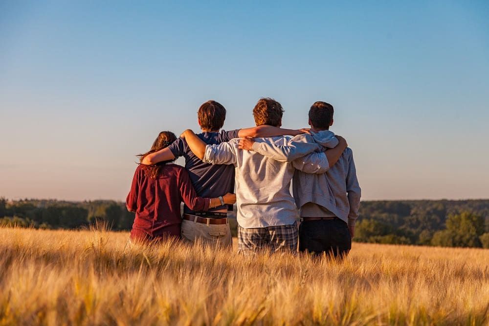 Vier Jugendliche stehen in einem Kornfeld und halten sich in den Armen